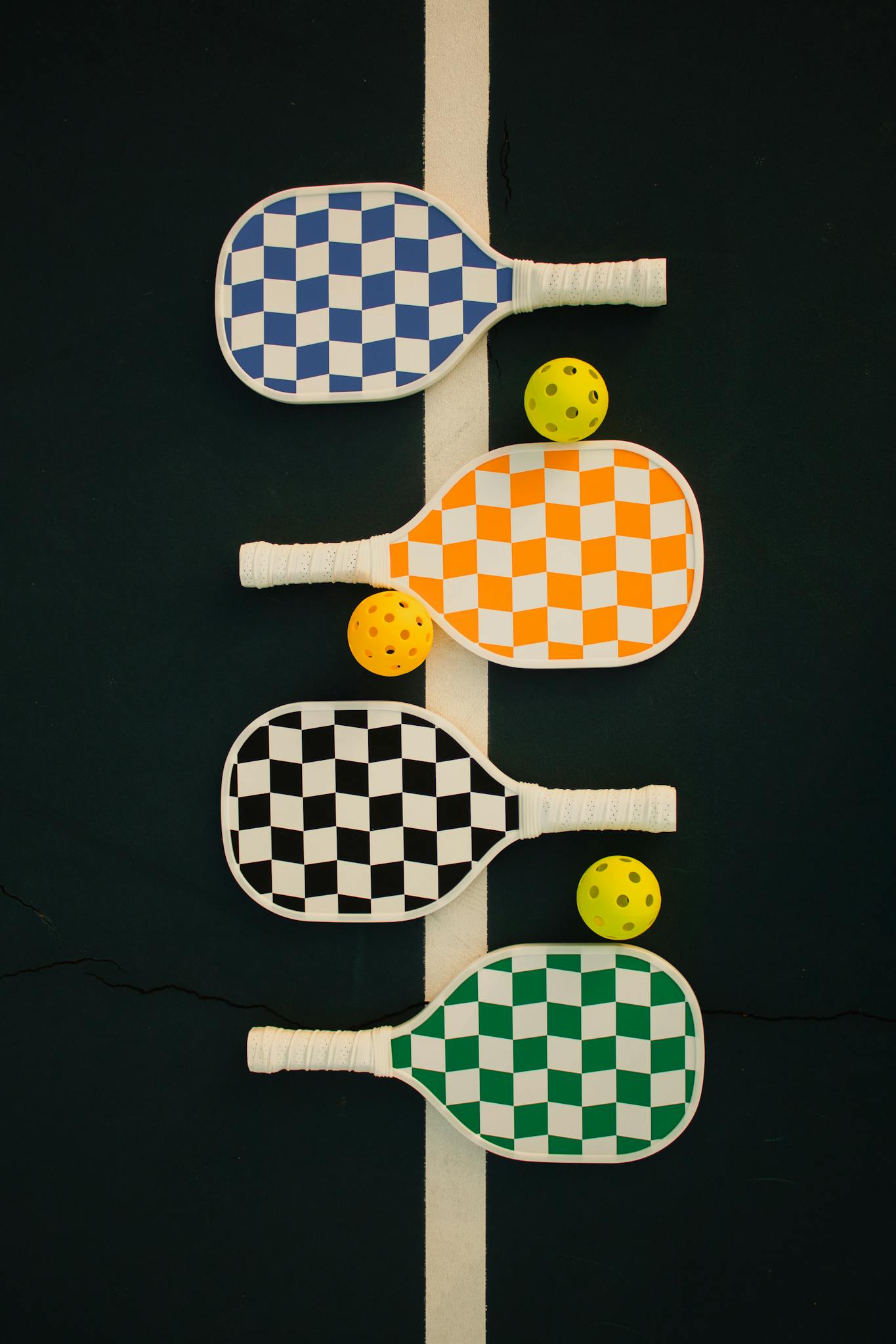 Close-up of four checkered pickleball paddles with matching balls on a court line.